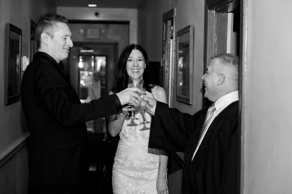 Black-and-white candid photograph of Sabrina and Nate sharing a champagne toast with wedding officiant France Krazalkovich after their ceremony.